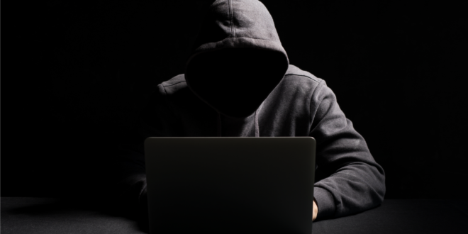 un hacker à capuche sans visage avec un laptop devant un fond noir